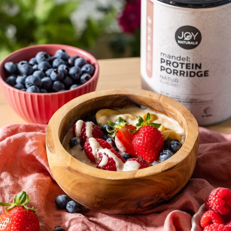 JOY NATURALS Mandel Protein Porridge Natur mit einem Topping aus Früchten und Mandelmus.